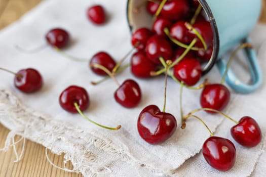 Fresh juicy sweet cherries in old rusty mug. Rustic background with homespun napkin.