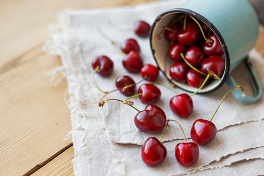 Fresh juicy sweet cherries in old rusty mug. Rustic background with homespun napkin.