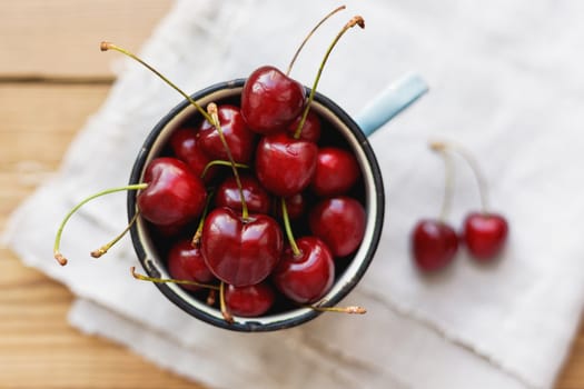 Fresh juicy sweet cherries in old rusty mug. Rustic background with homespun napkin.