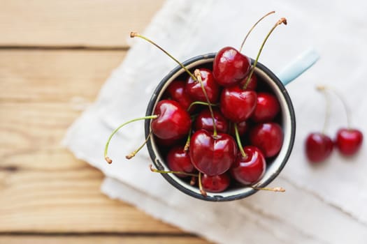 Fresh juicy sweet cherries in old rusty mug. Rustic background with homespun napkin.