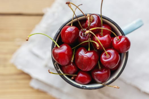 Fresh juicy sweet cherries in old rusty mug. Rustic background with homespun napkin.