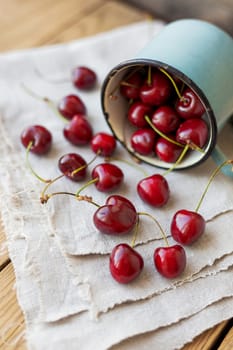 Fresh juicy sweet cherries in old rusty mug. Rustic background with homespun napkin.