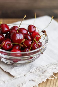 Fresh juicy sweet cherries in glass bowl. Rustic background with homespun napkin.