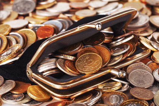Black wallet with different coins. Big heap of shiny coins as background.