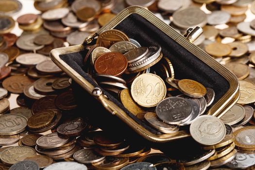 Black wallet with different coins. Big heap of shiny coins as background.