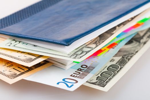 Different banknotes between pages of daily planner. Dollars and euro currency in diary.