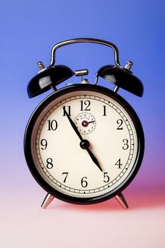 Black old fashioned alarm clock on blue background.