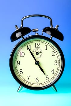 Black old fashioned alarm clock on blue background.