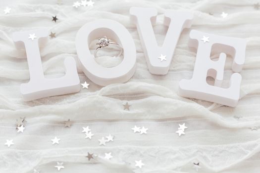 Word LOVE on white fabric background with engagement diamond ring. Good for Valentine's day cards. Place for text.