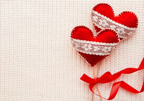 White woven background with two felt hearts with laces, symbol of love. Good for Valentine's Day cards. Place for text.