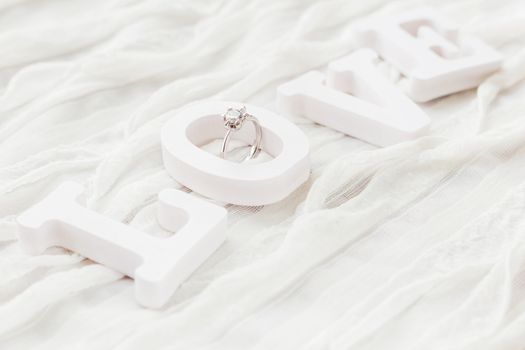 Word LOVE on white fabric background with engagement diamond ring. Good for Valentine's day cards.