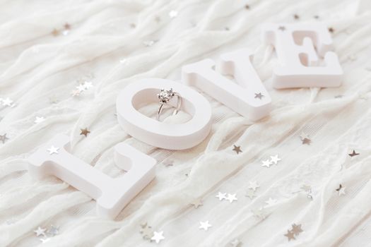 Word LOVE on white fabric background with engagement diamond ring. Good for Valentine's day cards.