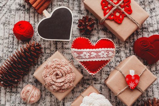 Valentine's Day symbols - hearts, presents in craft paper with crochet flowers, pine cones, red jewelry gift box - on knitted background.