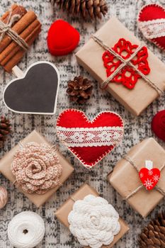 Valentine's Day symbols - hearts, presents in craft paper with crochet flowers, pine cones, red jewelry gift box - on knitted background.