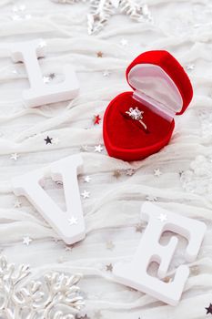 Word LOVE on white fabric background with engagement diamond ring in red gift box. Good for Valentine's day cards.