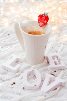 White cup of hot coffee with decorative heart and engagement diamond ring, symbol of love and marriage. Valentine's day background with lights and decorations.