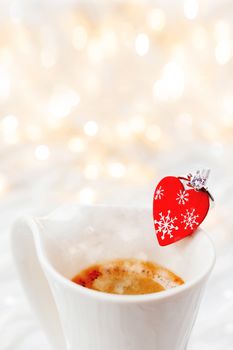 White cup of hot coffee with decorative heart and engagement diamond ring, symbol of love and marriage. Valentine's day background with lights and decorations.