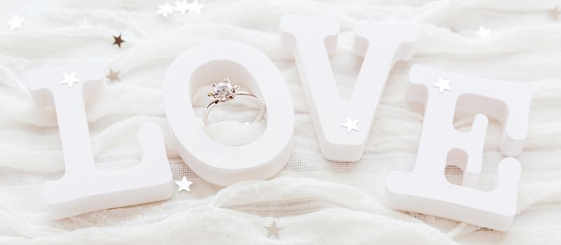 Word LOVE on white fabric background with engagement diamond ring. Good for Valentine's day cards. Place for text.
