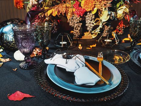 Table served in Halloween style. Bouquet with red flowers, decorative spiders, pumpkins with lettering and gothic vine glasses on black tablecloth. Holiday decorations.