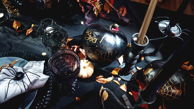 Table served in Halloween style. Bouquet with red flowers, decorative spiders, pumpkins with lettering and gothic vine glasses on black tablecloth. Holiday decorations.