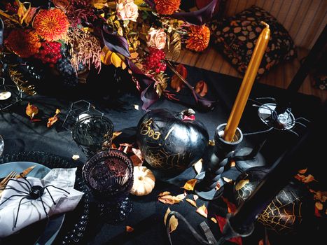 Table served in Halloween style. Bouquet with red flowers, decorative spiders, pumpkins with lettering and gothic vine glasses on black tablecloth. Holiday decorations.