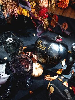 Table served in Halloween style. Bouquet with red flowers, decorative spiders, pumpkins with lettering and gothic vine glasses on black tablecloth. Holiday decorations.