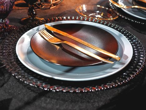 Table served in Halloween style. Gothic vine glasses and plates on black tablecloth. Holiday decorations.