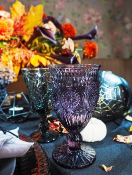 Table served in Halloween style. Bouquet with red flowers, decorative spiders, pumpkins with lettering and gothic vine glasses on black tablecloth. Holiday decorations.