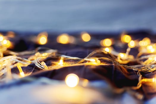 Defocused light bulbs, blurred colorful bokeh background. Holiday colorful lights on textile background. Cozy home decoration.