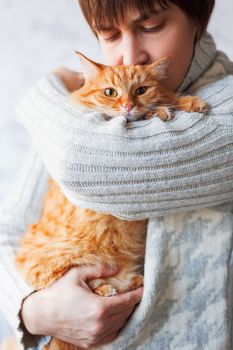 Man in knitted sweater holding cute ginger cat. Pet adoption. Stray cat how has home. Fluffy animal looks puzzled.