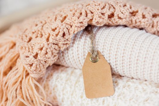Pile of beige knitted clothes. Crochet warm scarfs and sweaters are folded in one heap. Place for text on clear tag.