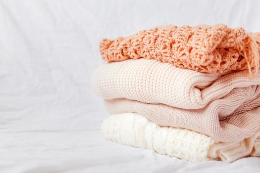Pile of beige woolen clothes on a white background. Warm knitted sweaters and scarfs are folded in one heap.