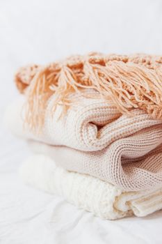 Pile of beige woolen clothes on a white background. Warm knitted sweaters and scarfs are folded in one heap.