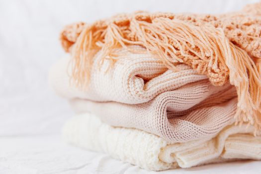 Pile of beige woolen clothes on a white background. Warm knitted sweaters and scarfs are folded in one heap.