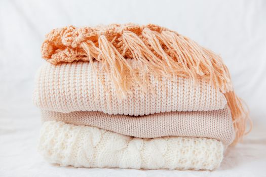 Pile of beige woolen clothes on a white background. Warm knitted sweaters and scarfs are folded in one heap.