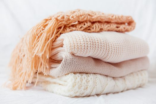 Pile of beige woolen clothes on a white background. Warm knitted sweaters and scarfs are folded in one heap.