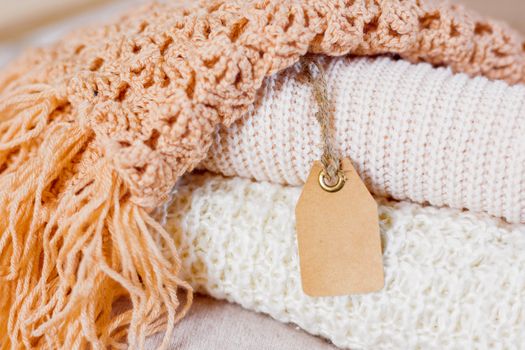 Pile of beige knitted clothes. Crochet warm scarfs and sweaters are folded in one heap. Place for text on clear tag.