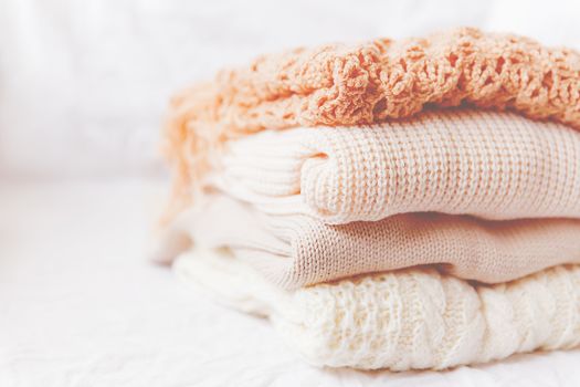 Pile of beige woolen clothes on a white background. Warm knitted sweaters and scarfs are folded in one heap. Imitation of Instagram style tone.
