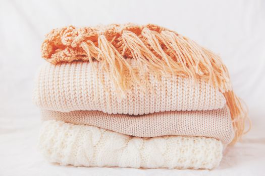 Pile of beige woolen clothes on a white background. Warm knitted sweaters and scarfs are folded in one heap. Imitation of Instagram style tone.