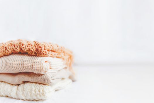 Pile of beige woolen clothes on a white background. Warm knitted sweaters and scarfs are folded in one heap. Place for text.