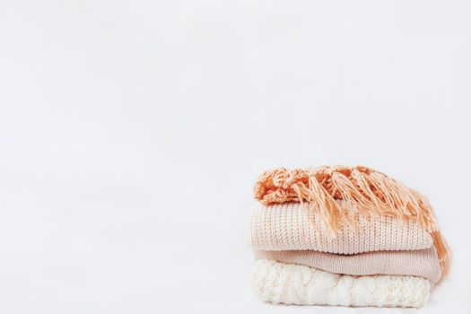Pile of beige woolen clothes on a white background. Warm knitted sweaters and scarfs are folded in one heap. Place for text.