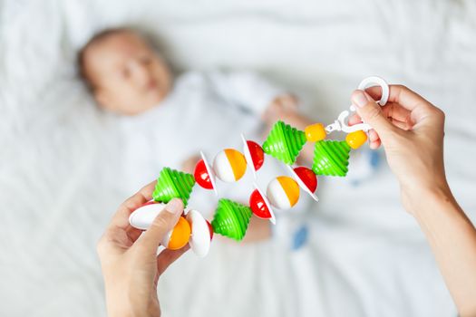 Woman holding baby's first toy - colorful rattle garland toy. Little kid on background.