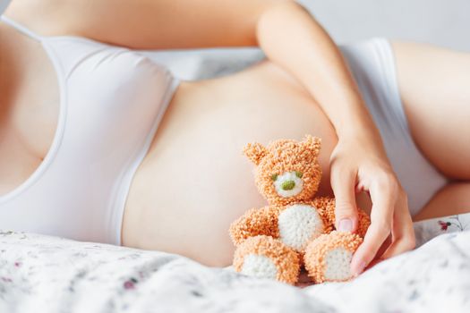 Pregnant woman in white underwear with toy bear. Young woman expecting a baby.