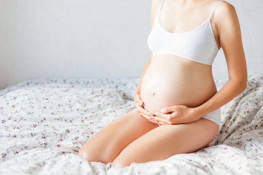 Pregnant woman in white underwear on bed. Young woman expecting a baby.