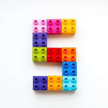 Number Five made of colorful constructor blocks. Toy bricks lying in order, making number 5. Education process - learning numbers with child using multicolored toy details.