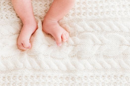 Baby's feet on white knitted background. Little child's bare feet. Cozy morning bedtime at home. Place for text.