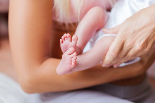 Mother holds newborn baby's bare heels. Tiny feet in woman's hand. Cozy morning at home.