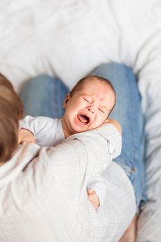 Woman holding a crying child. Mother comforts her little son or daughter. Baby with a big birthmark on his forehead.