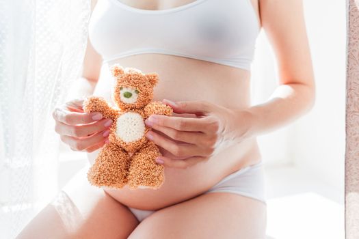 Pregnant woman in white underwear with toy bear. Young woman expecting a baby.