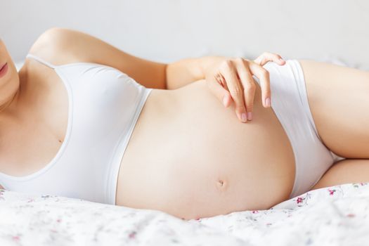 Pregnant woman in white underwear on bed. Young woman expecting a baby.